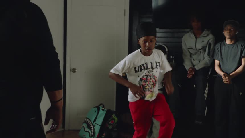 A talented young boy shows off his high-energy hip-hop dance moves while his friends watch from the background