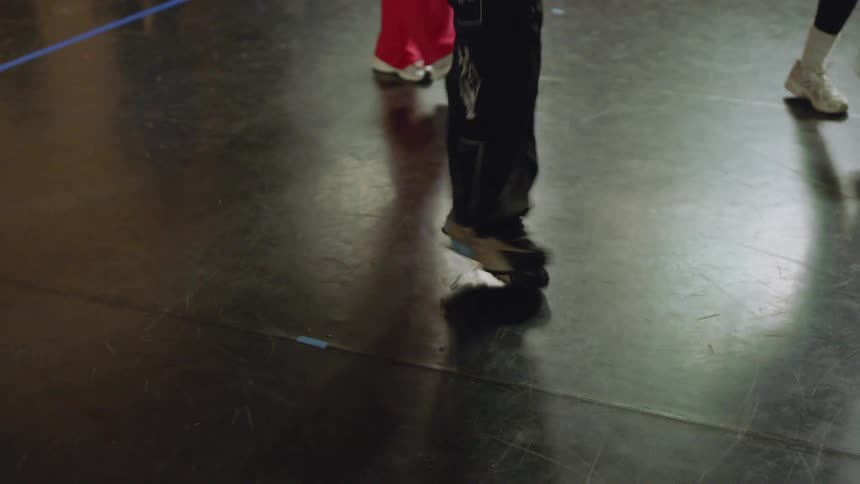 Slow motion tilt-up from a dancer's fast-moving feet to their upper body during a hip-hop dance class in a studio