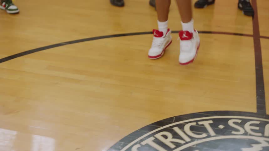 A talented young boy breakdances in the middle of a circle of friends and family on a basketball court