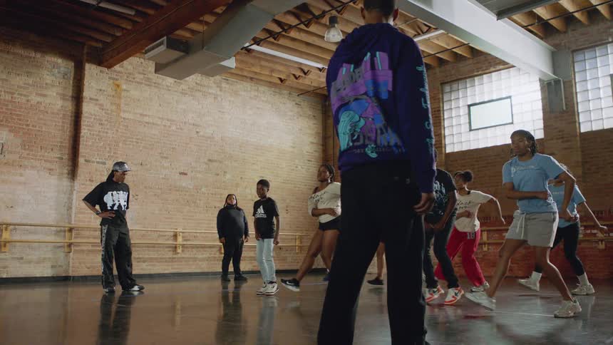 A diverse group of young people practice intricate footwork dance moves in slow motion during a class in an urban dance studio