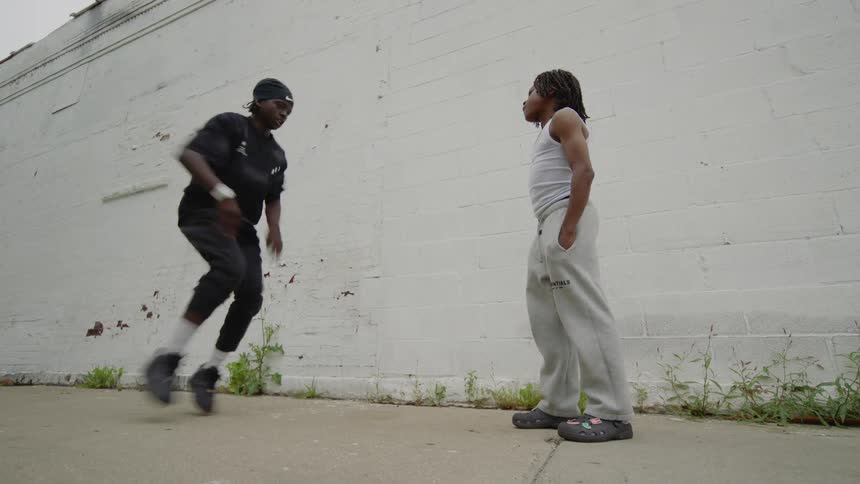 Two energetic young men take turns showcasing their impressive street dance moves in a friendly dance-off on a city sidewalk