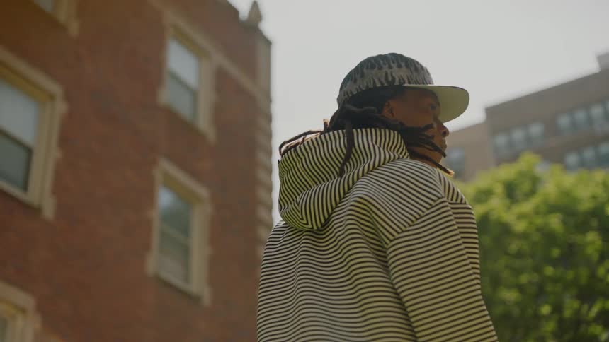 A cool young man with dreadlocks wearing a striped hoodie dances in slow motion on a sunny day in the city