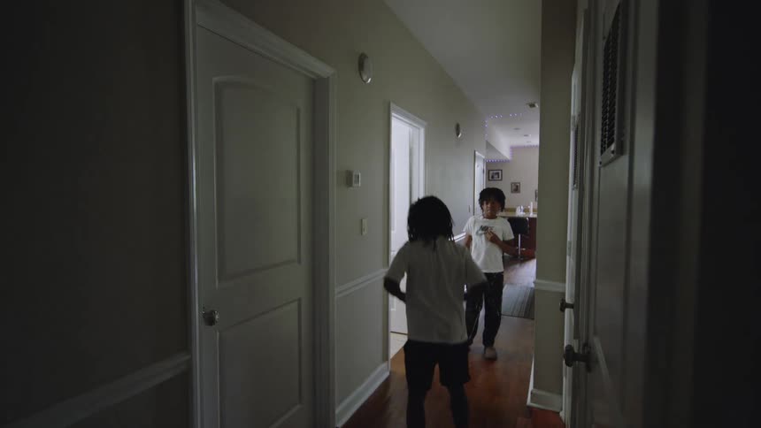 Two young brothers dance playfully in the dimly lit hallway of their home in slow motion