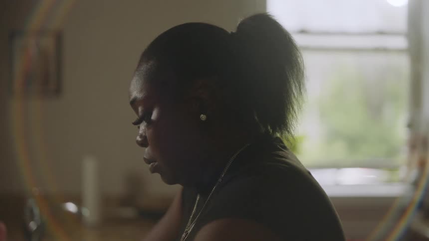 Close-up profile of a pensive woman looking down, backlit by a window with a lens flare