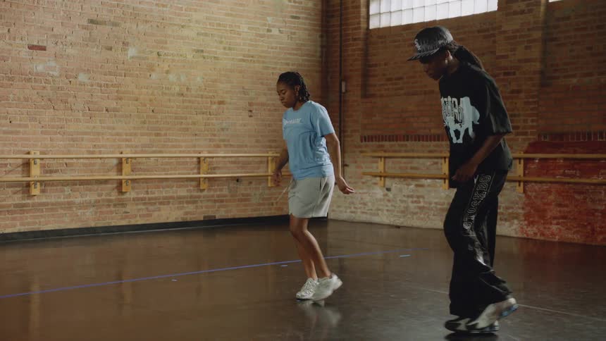 Two dancers practice complex hip-hop footwork together in a dance studio, captured in slow motion