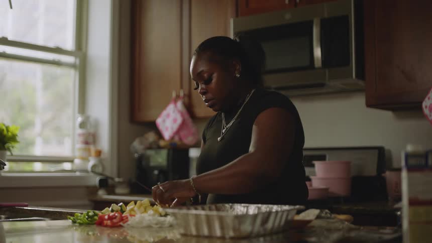 A woman carefully chops and mixes fresh vegetables into a foil pan while preparing a meal in her kitchen