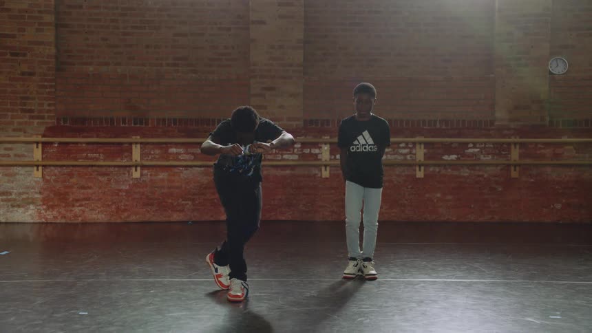 Two young Black boys practice energetic hip-hop dance routines in a sunlit studio in slow motion