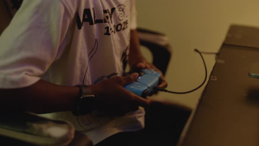 A young Black boy is focused and engaged while playing a video game at his desk in a dimly lit room