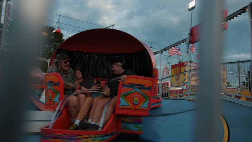 A colorful spinning ride whisks happy fairgoers around as seen from behind a fence at dusk