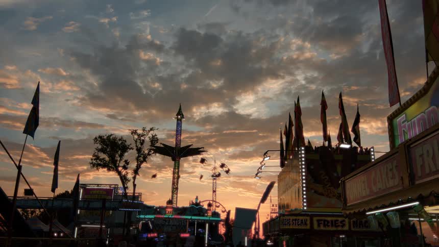 Carnival rides and food stands are silhouetted against a beautiful and dramatic cloudy sunset