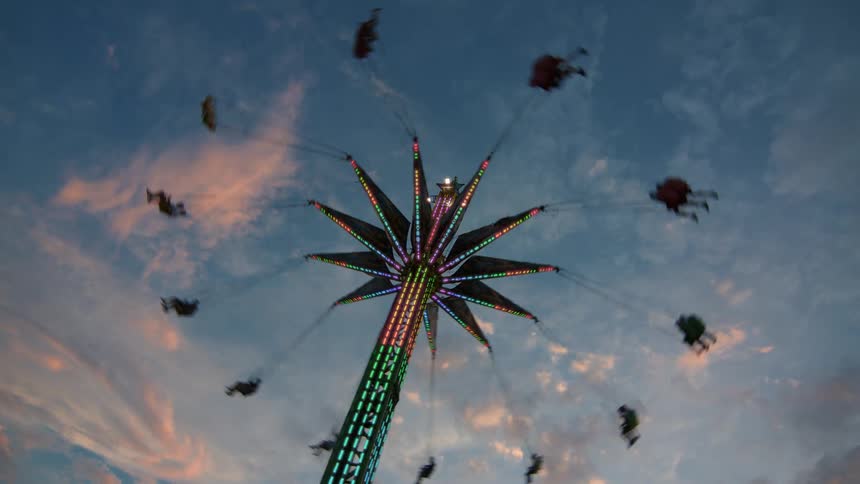 A colorful, star-shaped swing ride spins people high in the air against a beautiful sunset sky