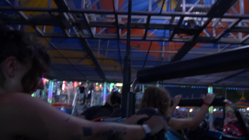 Energetic slow motion footage shows a tattooed woman laughing on a spinning bumper car ride at a carnival