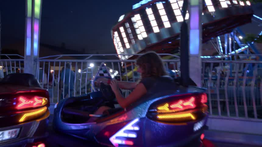 Slow motion shot of women laughing and having fun while driving colorful bumper cars at a lively amusement park at night