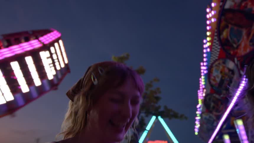 Slow motion shot of two young women laughing and enjoying the colorful lights of the carnival rides at night