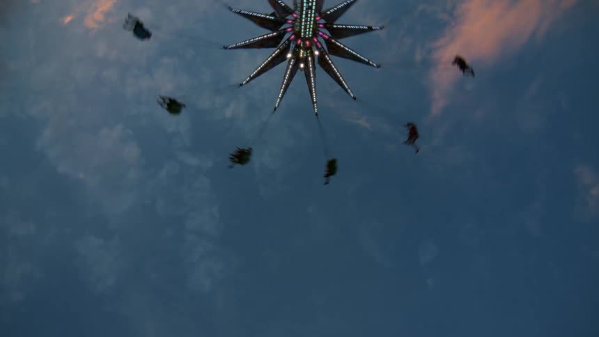 A colorful, lit-up swing ride spins thrill-seekers around against the beautiful dusk sky at an amusement park