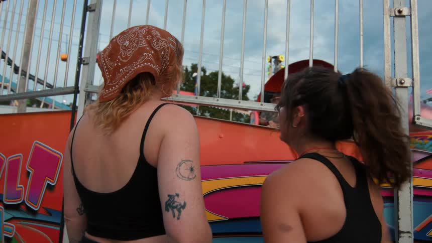 Slow motion shot of two friends chatting and smiling as they watch a carnival ride spin