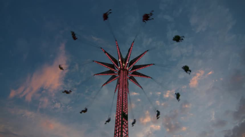 A brightly lit star flyer carnival ride spins guests high in the air during a colorful sunset