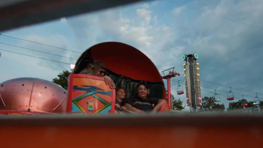 Three women laugh and smile together while riding a spinning amusement park ride in slow motion