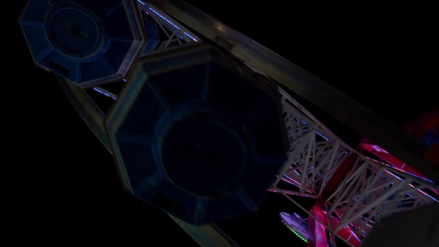 A low-angle, dutch tilt shot of a colorful Ferris wheel spinning at a carnival against the dark night sky