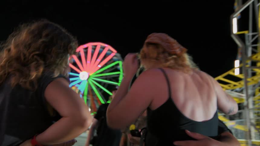Young friends have fun at a brightly lit carnival at night, surrounded by rides in slow motion