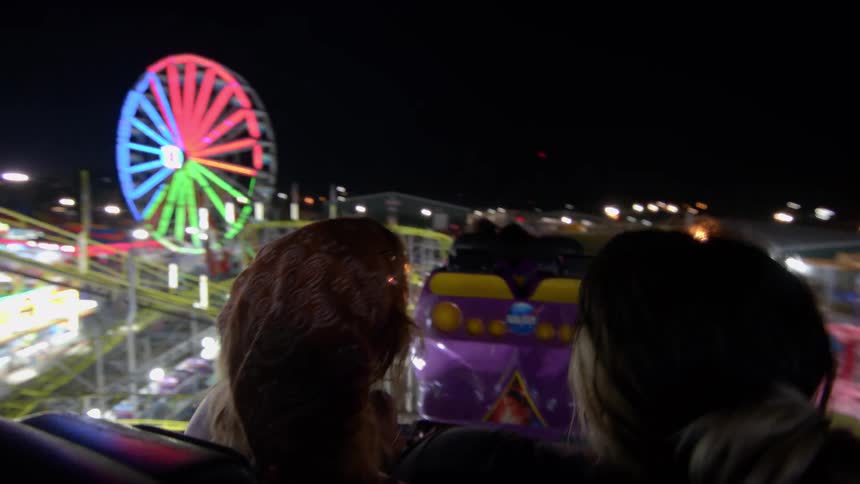 Friends enjoy a nighttime roller coaster ride with a thrilling point-of-view shot overlooking the vibrant amusement park