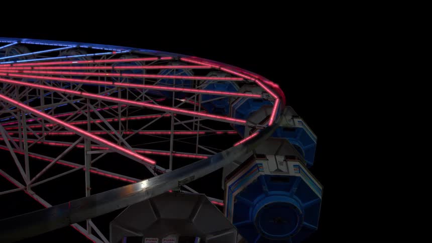 Colorful lights flash and change patterns on a stationary Ferris wheel at a carnival against the black night sky