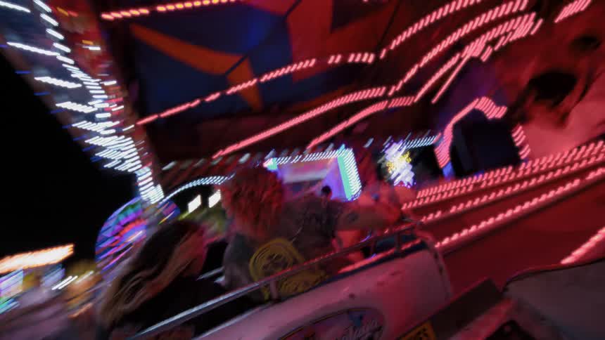 A thrilling point-of-view shot from behind a couple as they whip around on a fast carnival ride surrounded by a blur of neon lights