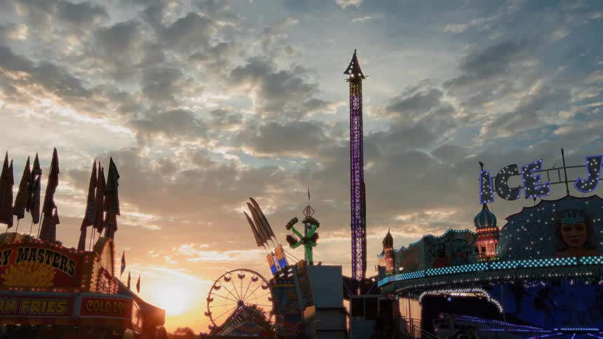 Thrilling carnival rides operate against a beautiful and cloudy sunset sky as crowds enjoy the fair
