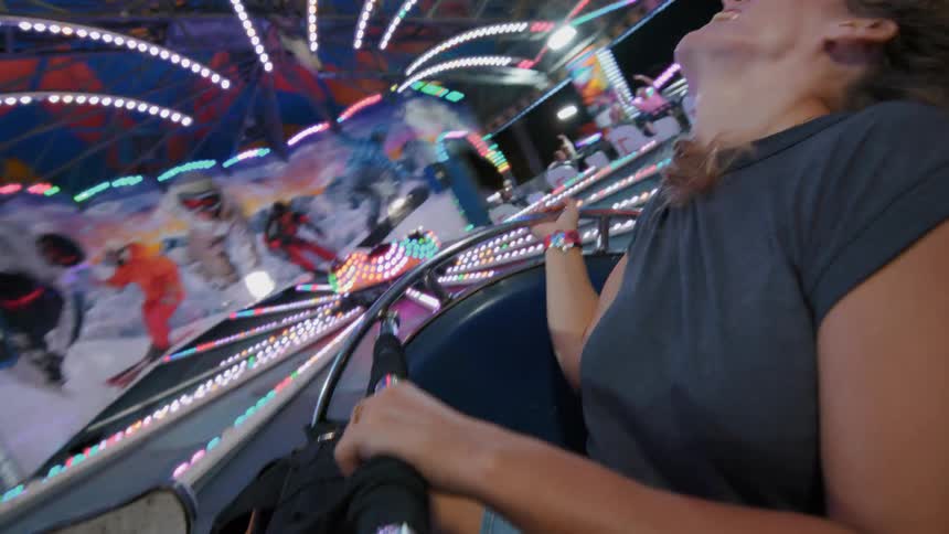 A joyful young woman with windblown hair enjoys a fast, colorful spinning ride at a nighttime carnival