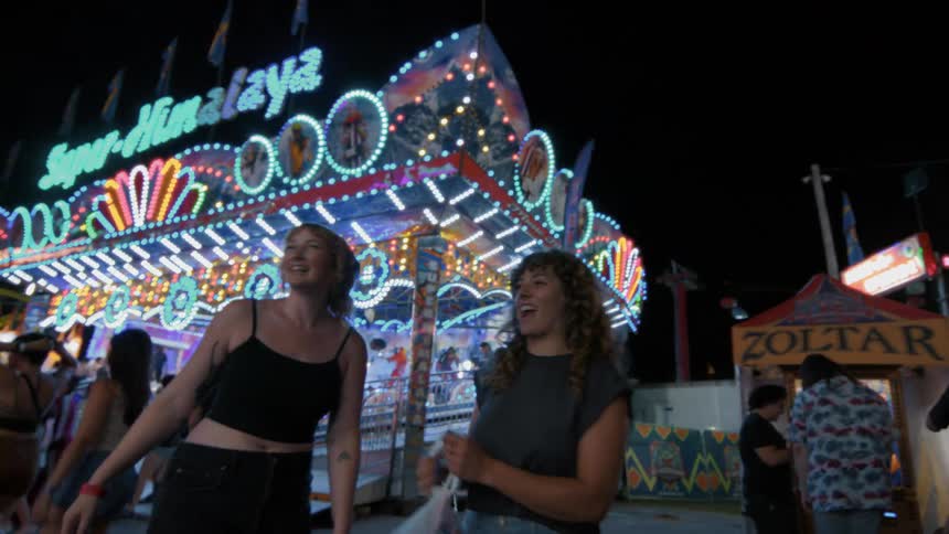 Two happy friends enjoy a fun night at the carnival, laughing in front of a brightly lit ride