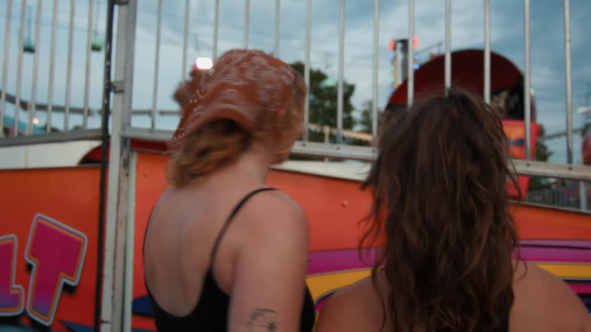 A young woman captures a video on her phone of her friends waving and smiling from a spinning ride at a carnival