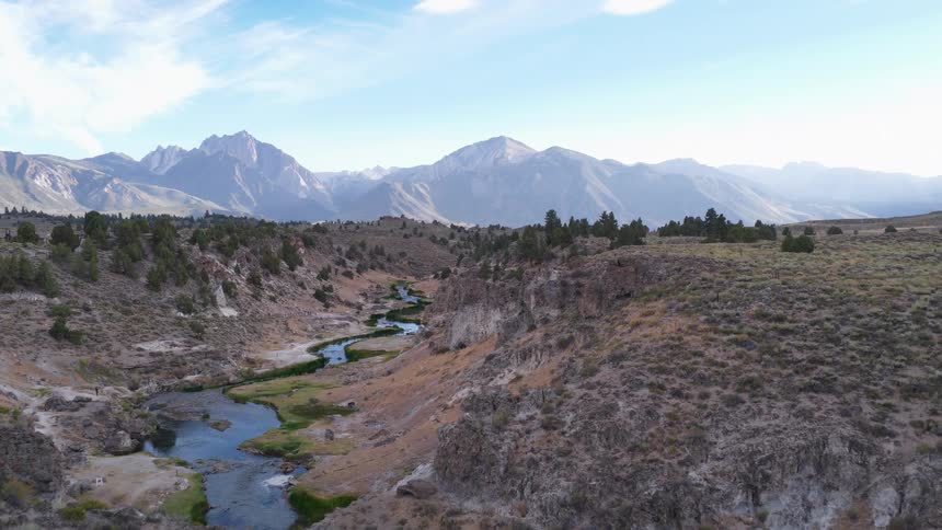 Sweeping aerial footage pulls back to reveal a scenic river canyon with the majestic Sierra Nevada mountain range on the horizon