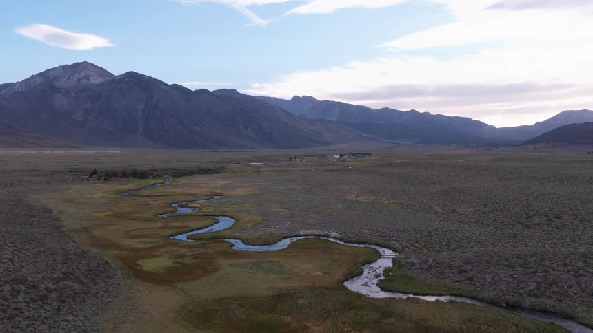 A serene aerial view captures a winding river flowing through a vast mountain valley during a peaceful sunrise