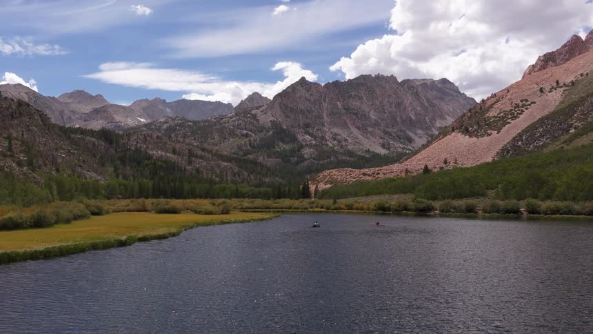 A serene mountain lake reflects the cloudy blue sky as people in small boats enjoy the majestic scenery