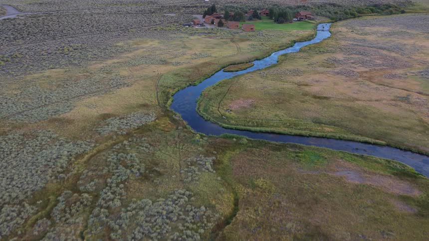Aerial view of a winding river in a vast valley, tilting up to reveal a remote lodge at the base of the Sierra Nevada mountains