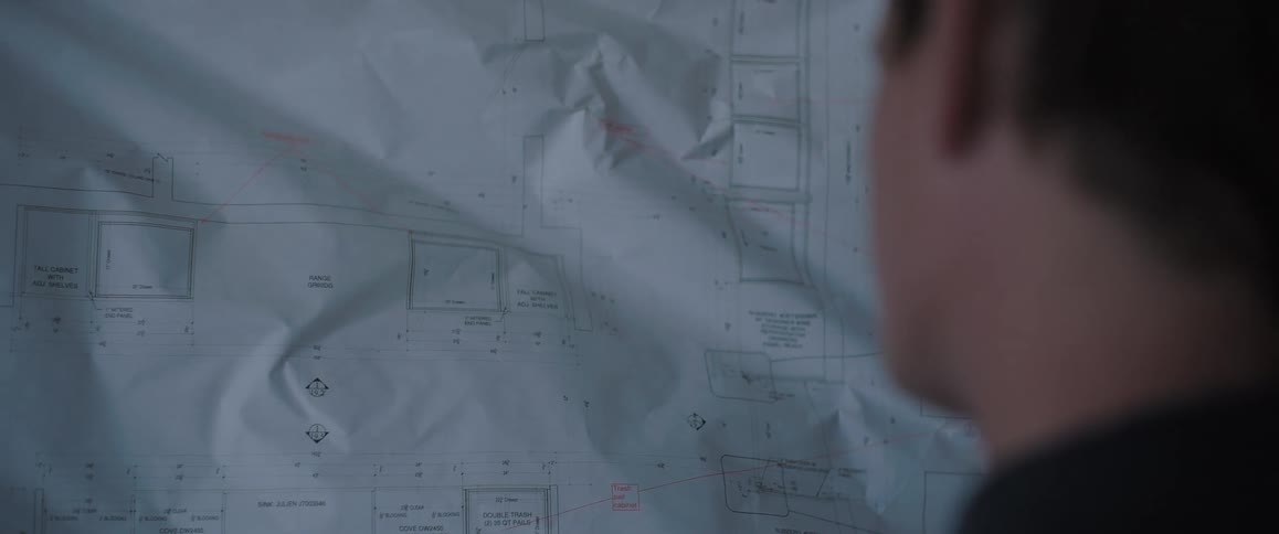 Over-the-shoulder shot of an architect unrolling and carefully examining architectural blueprints on a wooden wall