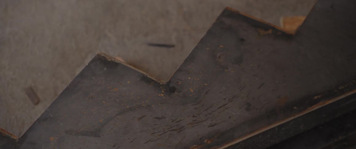 A close-up slow pan of a rusty, stair-shaped piece of metal resting on a concrete floor in an industrial setting