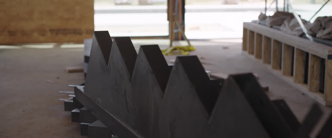 A close-up shot of a metal stair stringer resting on the concrete floor of a building under construction