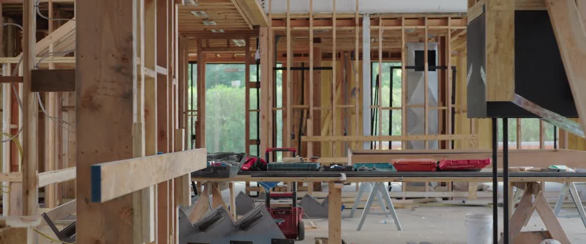 Slow pan across the interior of a house during its framing stage, showing exposed wooden beams and construction tools