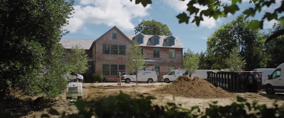 Wide view of a large residential house with construction and landscaping in the front yard on a sunny day