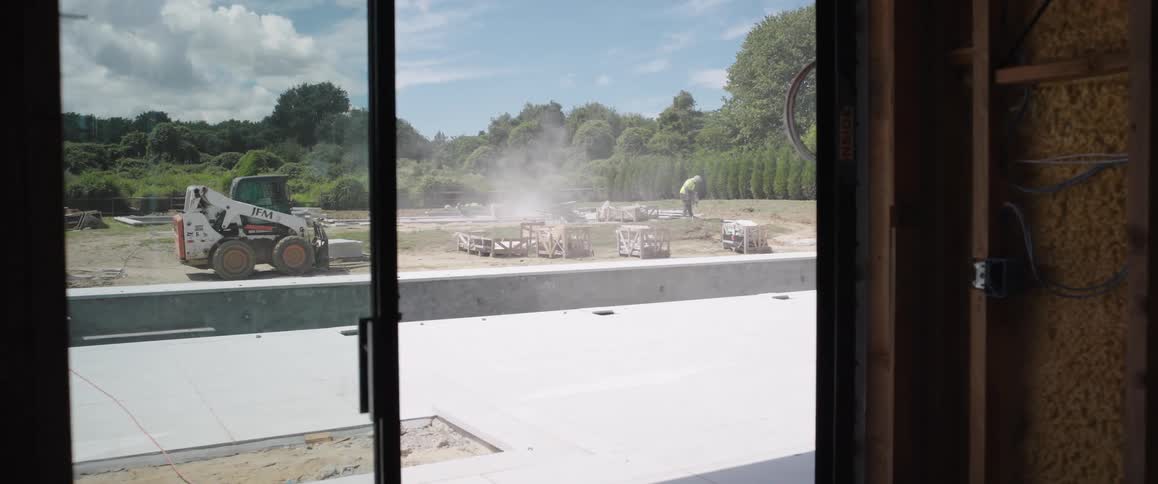 Slow zoom from an unfinished house through a glass door to a construction worker building a swimming pool in the backyard