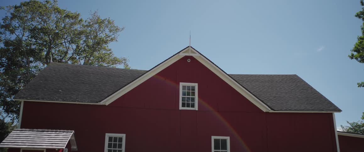 A beautiful rainbow lens flare appears on the side of a classic red barn on a bright, sunny day