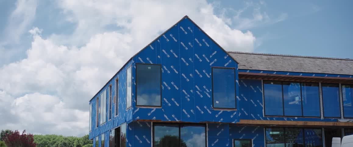 Time-lapse of clouds moving across the sky reflected in the windows of a modern house under construction