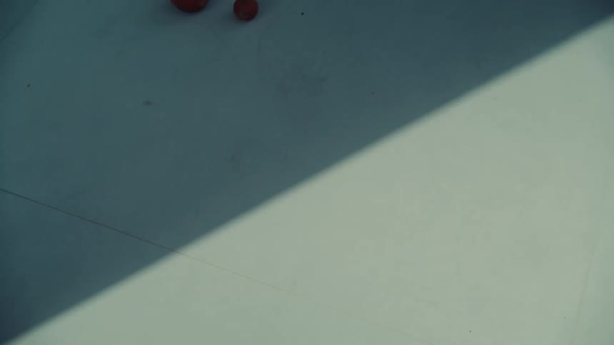 Slow motion top-down shot of red apples rolling from shadow into light on a white background