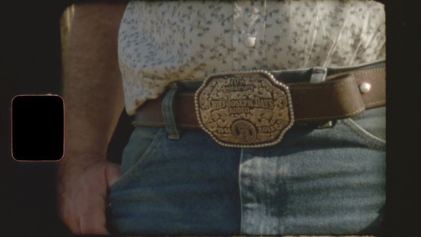Vintage-style footage shows a close-up of a man's large, decorative rodeo belt buckle