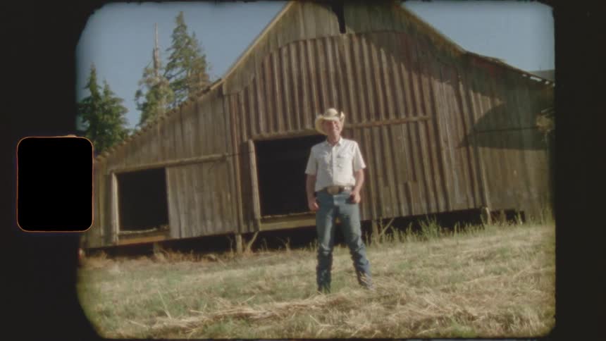 A cowboy stands proudly in front of a weathered wooden barn in this vintage 8mm style home movie
