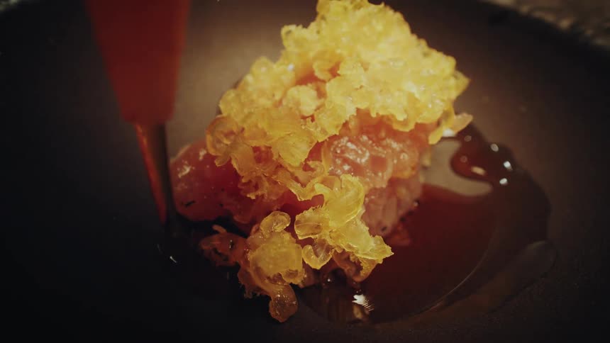 Extreme close-up of a chef finishing a beautifully plated gourmet dish with a savory sauce