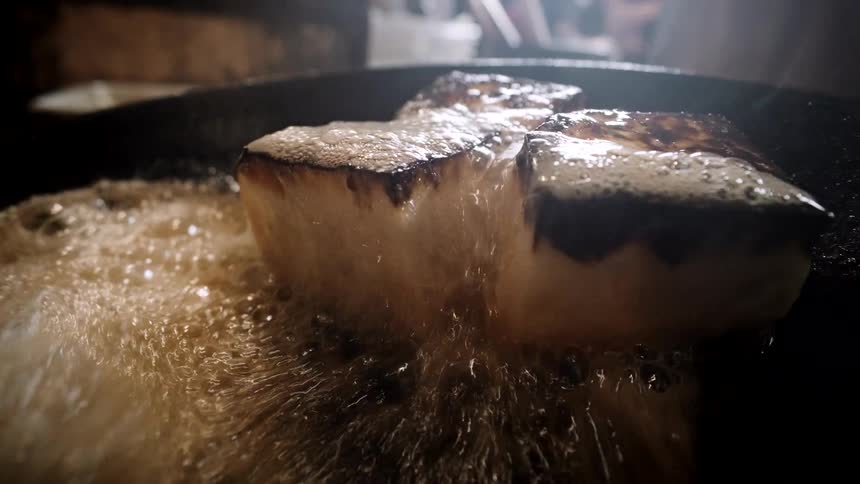 A chef continuously bastes thick pieces of pan-seared food with hot, bubbling butter in a dark skillet