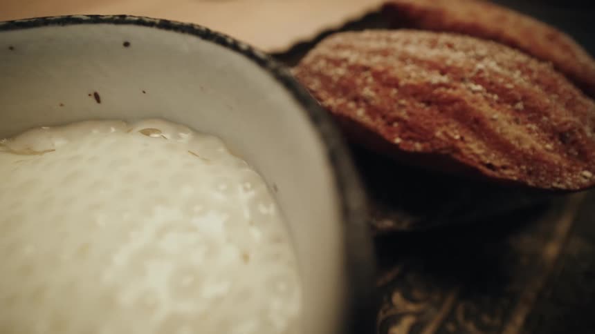 A decadent dessert of warm, bubbling tapioca pudding is served with classic French madeleines on a rustic platter