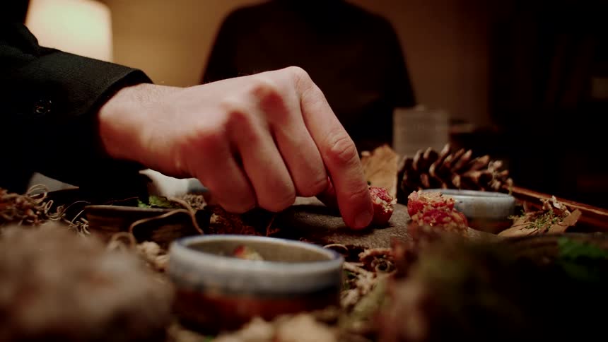 A person carefully picks up a delicate gourmet morsel from a rustic, nature-inspired food presentation in slow motion